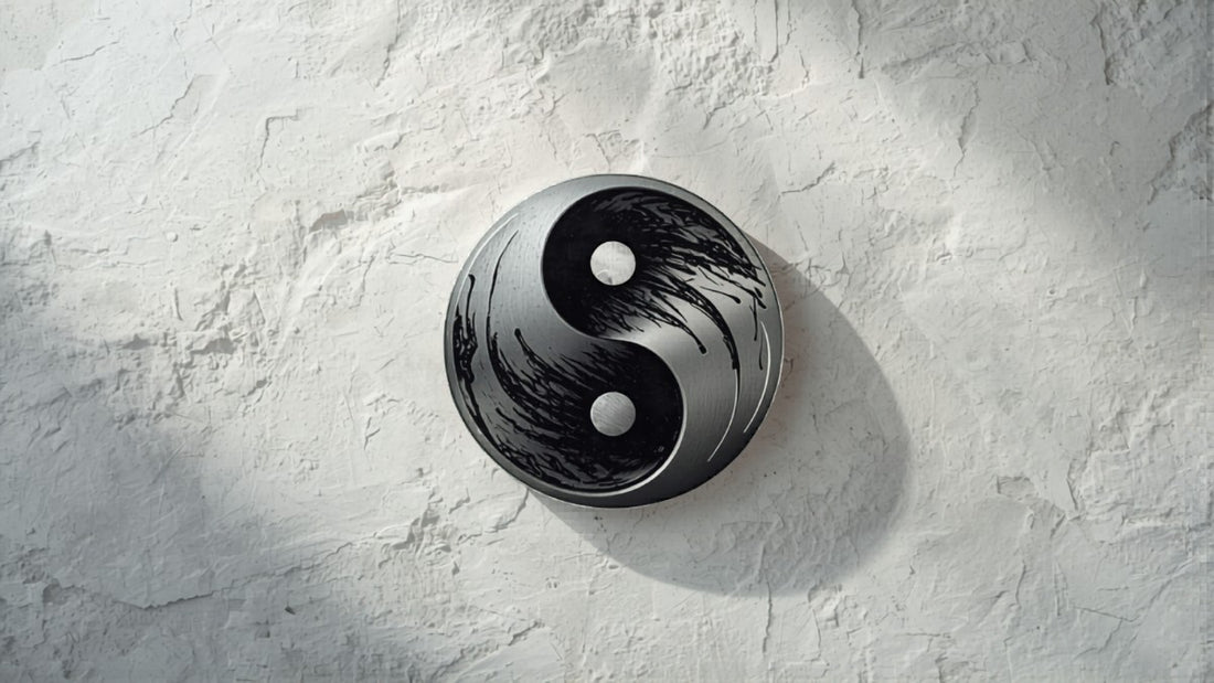 Minimalist yin yang symbol in brushed silver and black ink on white stone, editorial jewelry photography