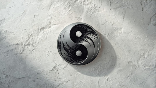 Minimalist yin yang symbol in brushed silver and black ink on white stone, editorial jewelry photography