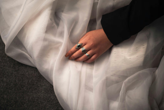 Close-up of multiple silver rings on a hand resting among delicate white flowers, soft natural light