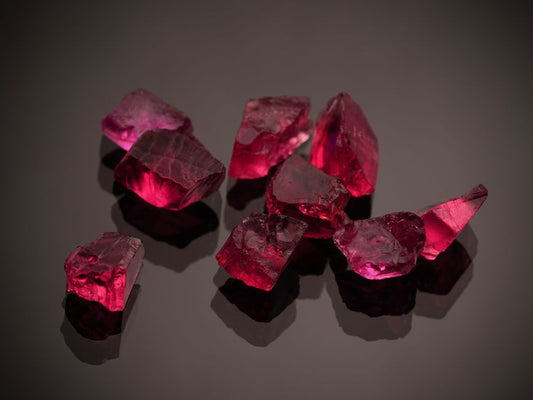 Cluster of faceted deep red ruby gemstones photographed close up on a dark background, showing vivid color