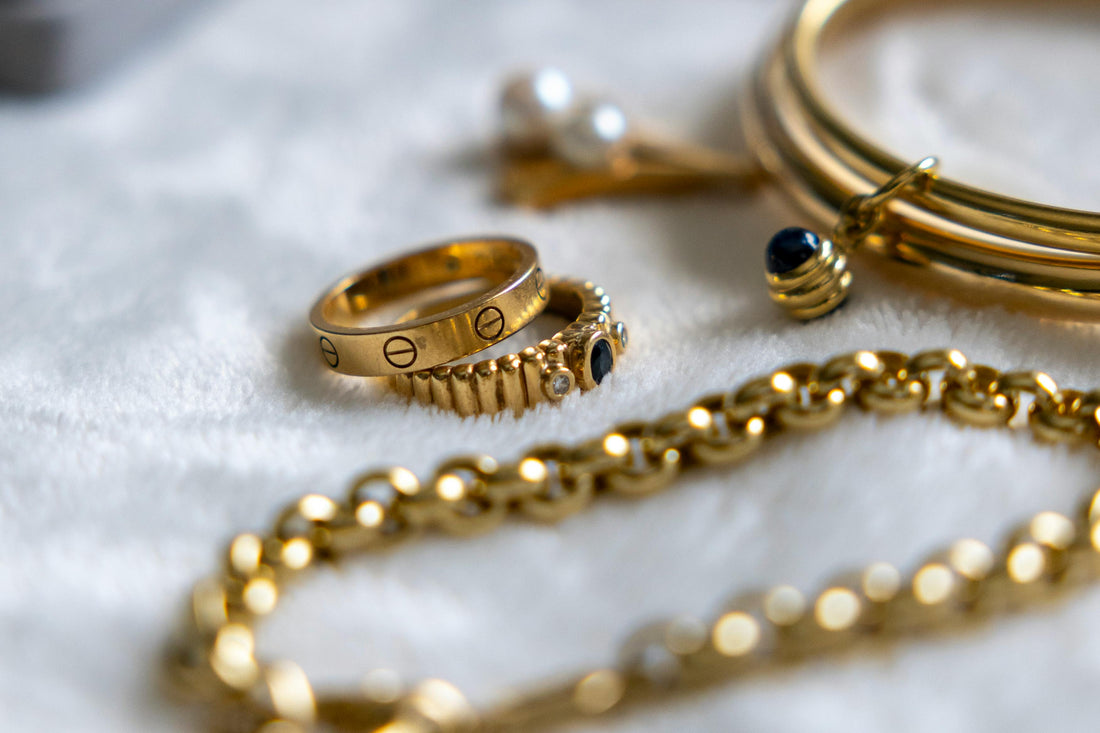 Collection of gold rings, bracelets, and chains with gemstones arranged on a textured surface