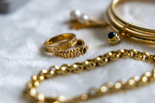 Collection of gold rings, bracelets, and chains with gemstones arranged on a textured surface