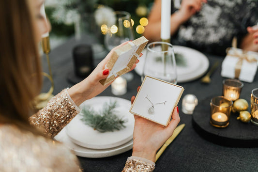 Woman opening a necklace gift box at a beautifully set holiday dinner table