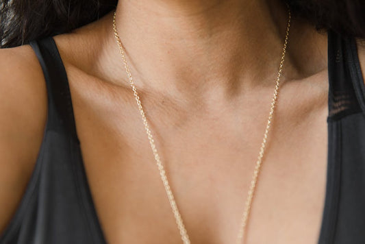 Layered necklaces in mixed metals — sterling silver and 14K gold pendants worn together at the collarbone, soft natural light