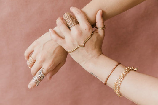 Stack of slim 14K gold birthstone rings worn on a hand in natural light, fine jewelry detail